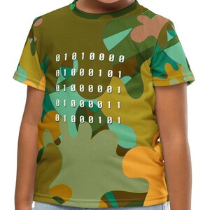 Op de afbeelding: Een kind draagt een T-shirt met een groene, gele en blauwe camouflageprint met een wit patroon van binaire code. Het shirt heeft korte mouwen en een ronde hals.