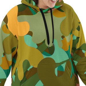 Op de afbeelding: Een hoodie met een kleurrijk abstract patroon in tinten groen, bruin en oranje. De hoodie heeft een voorzak en zwarte trekkoorden. Het kledingstuk is gemaakt van een zacht materiaal.