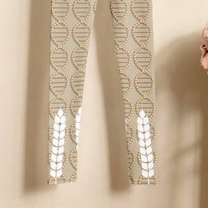 Può includere: Leggings beige con un motivo a spirale di DNA bianco e spighe di grano bianche in fondo a ciascuna gamba.