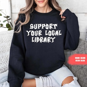 May include: Black sweatshirt with the text "SUPPORT YOUR LOCAL LIBRARY" in white, stylized in a metal band font.