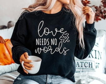 May include: Black sweatshirt with white text that reads "love needs no words" and a white puzzle piece with a heart in the center.