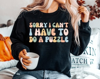 May include: A black sweatshirt with the text "SORRY I CAN'T I HAVE TO DO A PUZZLE" in colorful, rounded letters.
