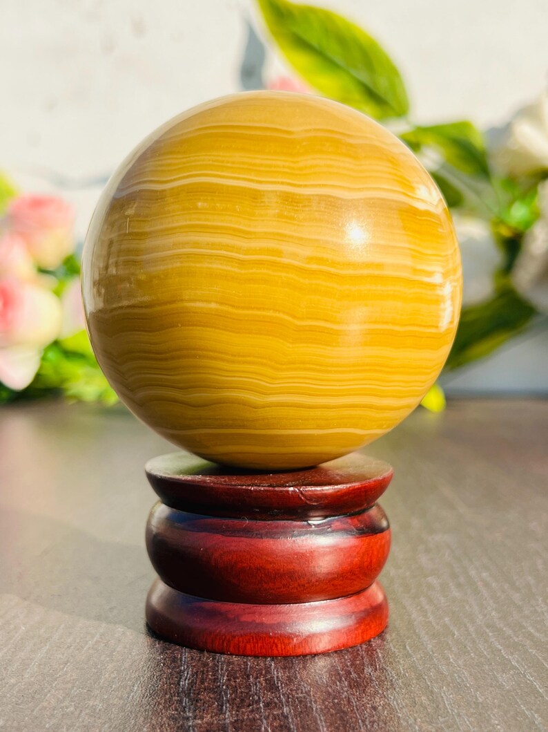 May include: A golden-yellow sphere with horizontal banding, displayed on a three-tiered, dark red wooden stand. The sphere has a polished, glossy finish. The stand is made of polished wood.