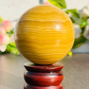 May include: A polished, golden-yellow sphere with banded patterns, displayed on a tiered, dark red wooden stand. The sphere's surface reflects light, showcasing its natural variations. The stand provides a stable base for this decorative object.
