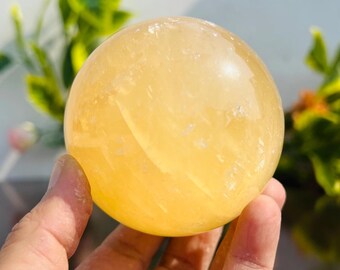 May include: A large, smooth, yellow calcite sphere. The sphere is polished and has a translucent appearance.