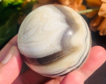 May include: A white and brown banded agate sphere with swirling patterns. The sphere is smooth and polished.