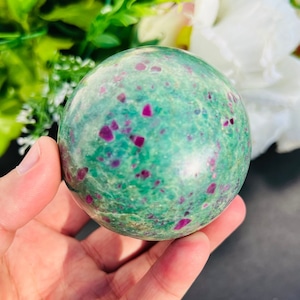 May include: A green and pink sphere with a smooth, polished surface. The sphere is made of a type of gemstone with a speckled pattern.
