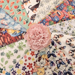 May include: A collection of colourful fabric swatches with various patterns, including watermelons, unicorns, frogs, butterflies, and cartoon characters. The fabrics are arranged in a circular pattern with a pink flower in the centre.