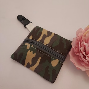 May include: A small camouflage zippered pouch with a black clip attached to a white strap. The pouch is made of fabric and has a zipper closure.