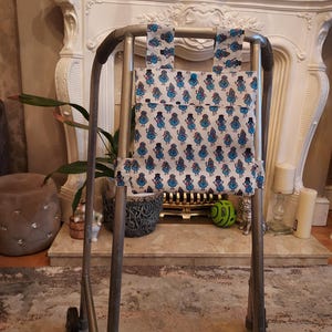 May include: A silver walking frame with a white fabric bag attached. The bag has a blue and white pattern of cartoon characters wearing hats.