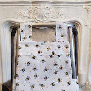 May include: A white walker bag with a bee and yellow dot pattern. The bag is attached to a silver walker.