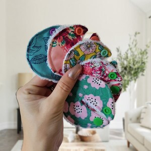 May include: A set of four reusable cloth menstrual pads with floral patterns and colourful buttons. The pads are made of soft, absorbent fabric and are designed to be comfortable and discreet.