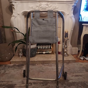 May include: A silver walking frame with a black and white striped fabric bag hanging from the top bar.