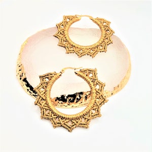 May include: A pair of gold hoop earrings with a delicate, intricate design. The earrings are made of a woven material and have a circular shape.