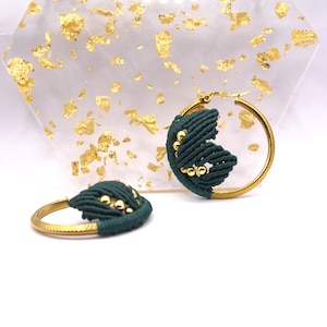 以下が含まれることがあります： 濃い緑色のマクラメ模様と金色のビーズが付いた、金色のフープイヤリングのペアです。