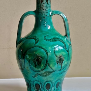 May include: A turquoise ceramic vase with two handles and a narrow neck. The vase features a floral design with black outlines and green leaves. The base and neck have decorative patterns. The vase is approximately 30 cm tall.
