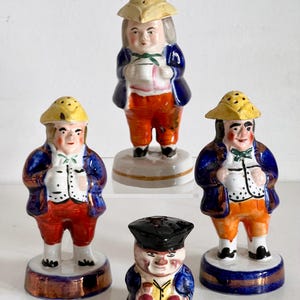 May include: Set of four vintage ceramic salt and pepper shakers featuring figures in colonial attire. The figures are painted in blue, red, yellow, and white. The shakers have a gold trim.