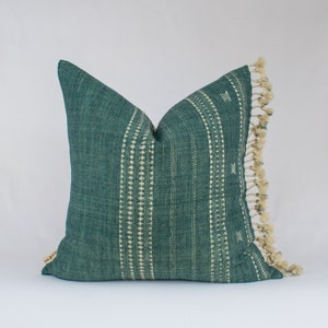 May include: A teal blue throw pillow with white geometric patterns and a fringe border.