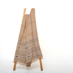 May include: A brown woven throw blanket with a geometric pattern and fringe. The blanket is draped over a wooden stool.