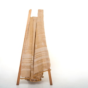 May include: A tan throw blanket with white stripes and tassels hangs on a wooden stand. The blanket is made of a soft, woven fabric.