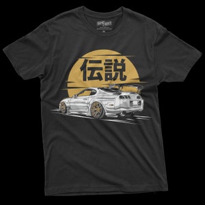May include: A black t-shirt with a white Toyota Supra car graphic and the Japanese word "伝説" (Legend) in gold lettering on a yellow sun graphic.