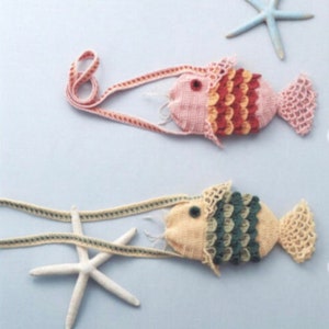 May include: Two crocheted fish purses with adjustable straps. The pink fish purse has red, orange, and yellow scales. The yellow fish purse has green scales. Both purses have a white crocheted trim.