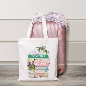 Könnte beinhalten: Weiße Canvas-Tragetasche mit einem floralen Design, das einen Stapel Bücher mit dem Text "Printemps" und "Jardin Secret" zeigt.