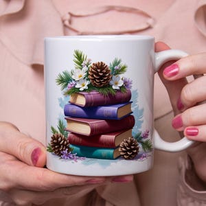 Peut inclure: Mug en céramique blanche avec un motif de livres empilés aux couleurs violettes, rouges et turquoise. Le motif comprend des fleurs blanches, des aiguilles de pin vertes et des pommes de pin brunes. La tasse a une anse blanche.
