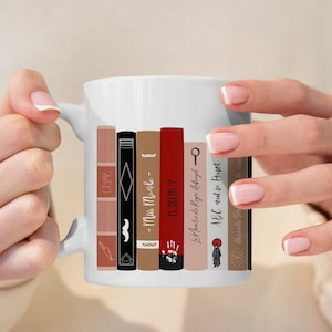 Könnte beinhalten: Weiße Keramiktasse mit einem Bücherregal-Design mit verschiedenen Buchtiteln, darunter "CRIME", "Miss Marple", "11.M.?", "Der Mord an Roger Ackroyd" und "A.B.C. gegen Poirot".