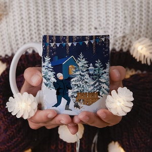 Könnte beinhalten: Eine weiße Keramiktasse mit einem Wintermotiv. Die Tasse zeigt eine Person, die einen Hund in einer schneebedeckten Landschaft mit einem Haus im Hintergrund spazieren führt. Die Szene spielt nachts mit funkelnden Lichtern und einem blauen Himmel.