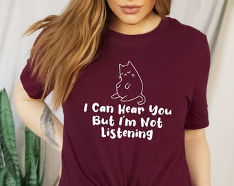 May include: A maroon t-shirt with a white outline of a cat and the text "I Can Hear You But I'm Not Listening".