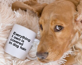 May include: A white ceramic mug with the text "Everything I own is covered in dog hair."  A golden brown dog is lying on a fluffy white blanket.