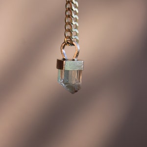 May include: A gold chain necklace with a clear crystal pendant. The pendant is set in a gold frame and has a faceted design.