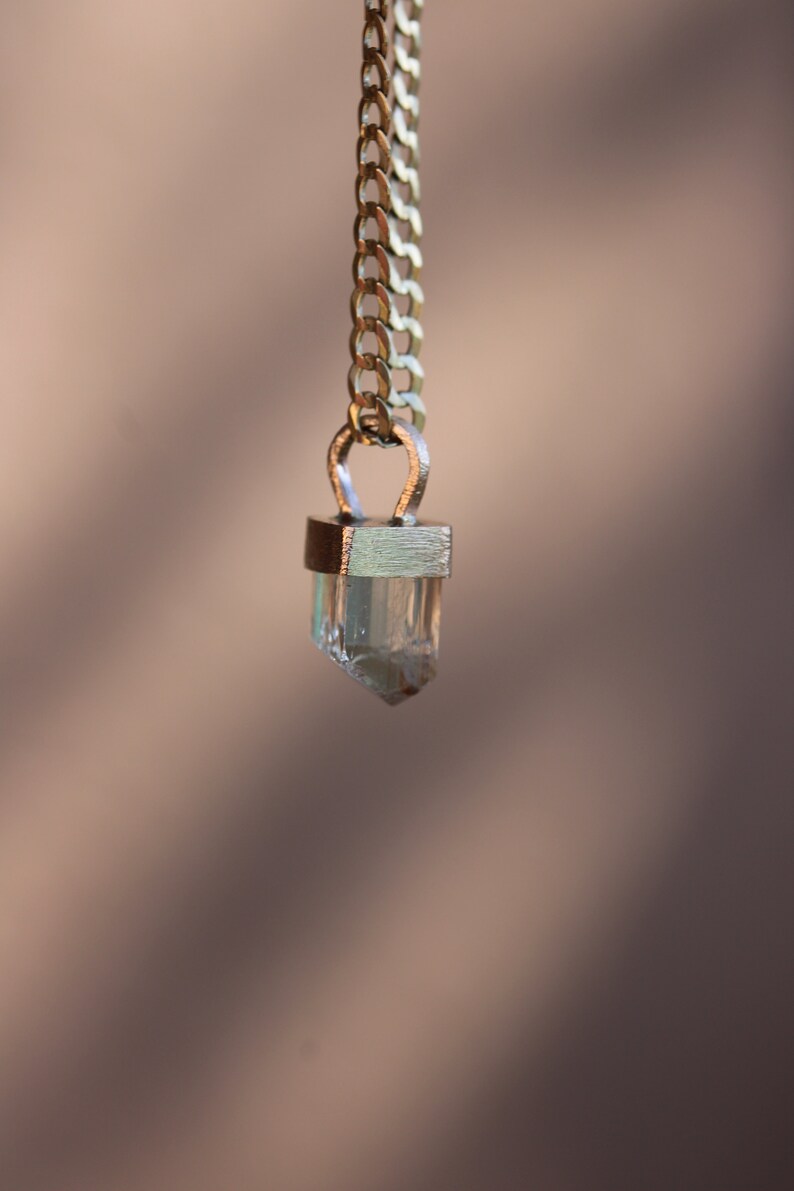 May include: A gold chain necklace with a clear crystal pendant. The pendant is set in a gold frame and has a faceted design.