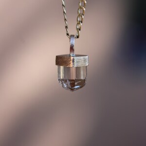 May include: A silver chain necklace with a clear crystal pendant. The pendant is set in a silver frame.