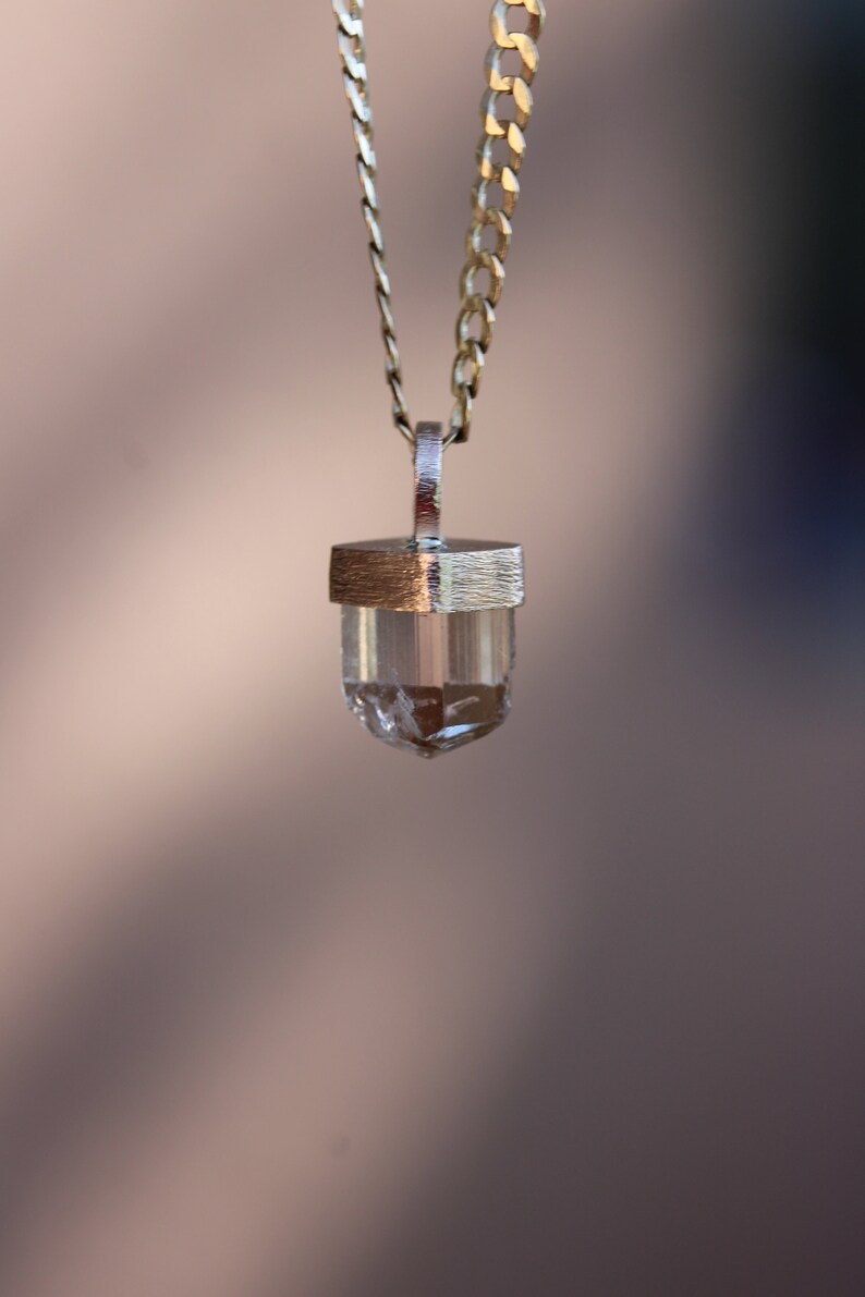 May include: A silver chain necklace with a clear crystal pendant. The pendant is set in a silver frame.