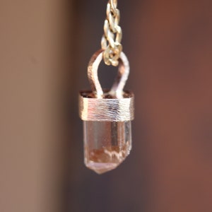 May include: A gold chain necklace with a clear crystal pendant. The crystal is set in a gold bezel and has a pointed tip.