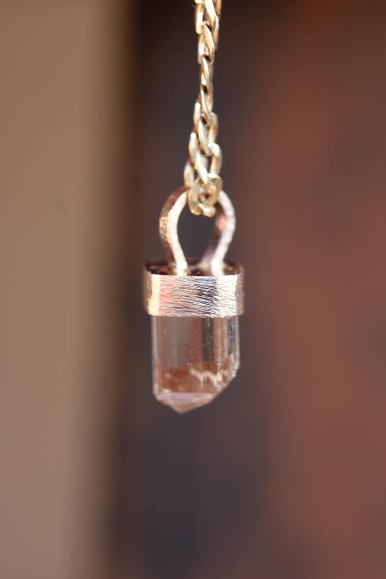 May include: A gold chain necklace with a clear crystal pendant. The crystal is set in a gold bezel and has a pointed tip.