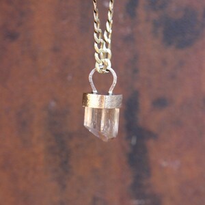 May include: A gold chain necklace with a clear crystal pendant. The pendant is set in a gold frame and has a simple, elegant design.