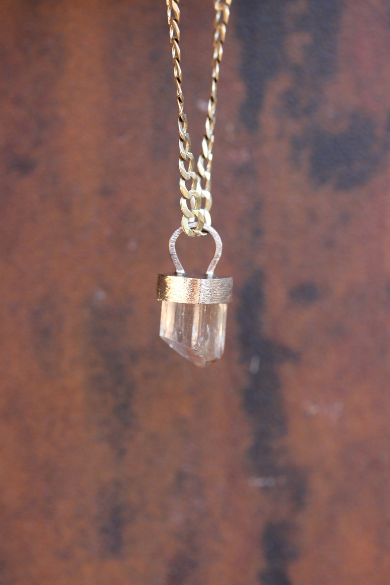 May include: A gold chain necklace with a clear crystal pendant. The pendant is set in a gold frame and has a simple, elegant design.