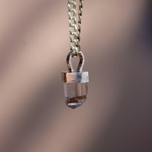 May include: A gold chain necklace with a clear crystal pendant. The pendant is set in a gold bezel and has a faceted shape.