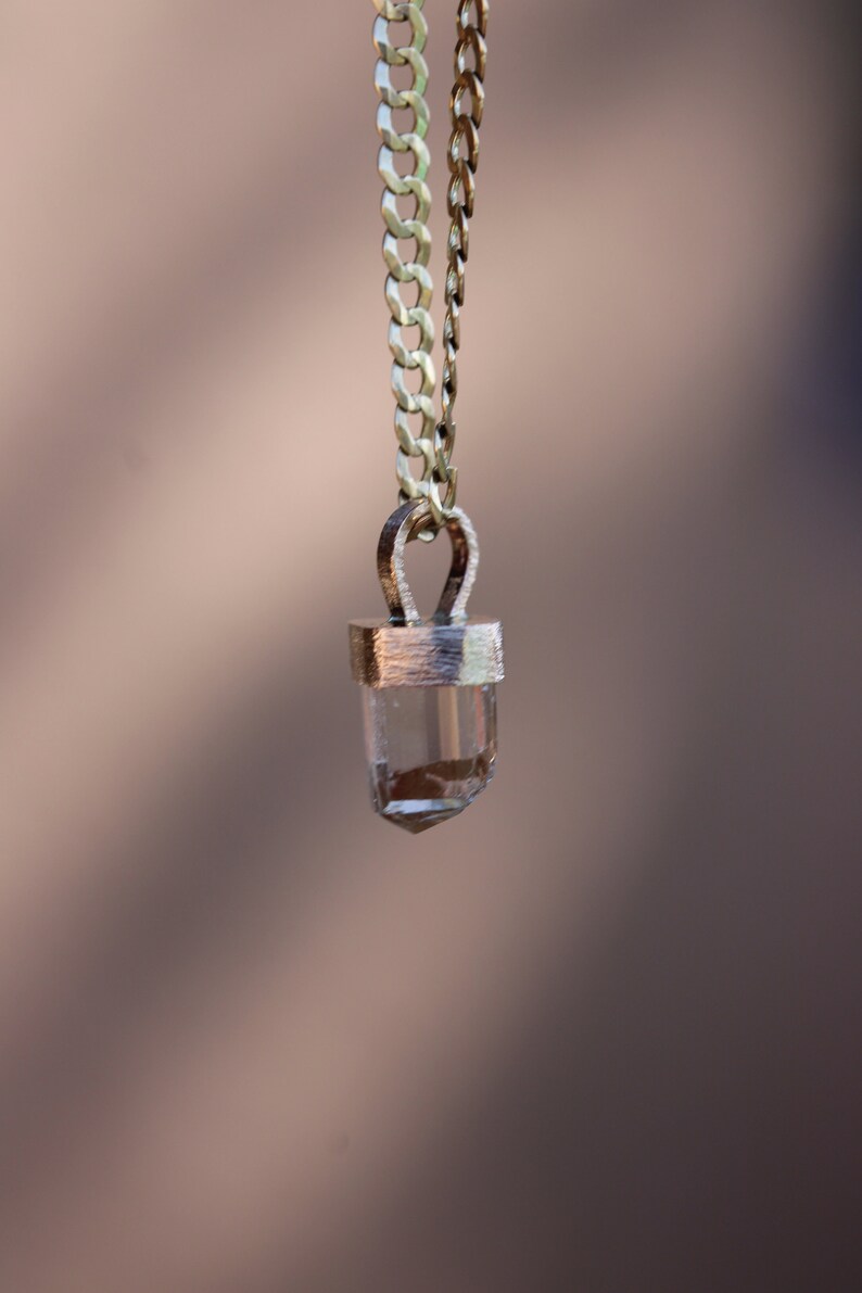 May include: A gold chain necklace with a clear crystal pendant. The pendant is set in a gold bezel and has a faceted shape.