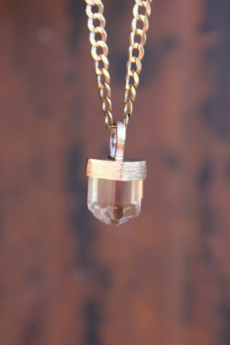 May include: A gold chain necklace with a clear quartz crystal pendant. The crystal is set in a gold bezel and has a faceted shape.