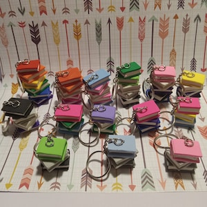 May include: A collection of colorful miniature book keychains. Each keychain features a stack of small, colorful books with a silver key ring.