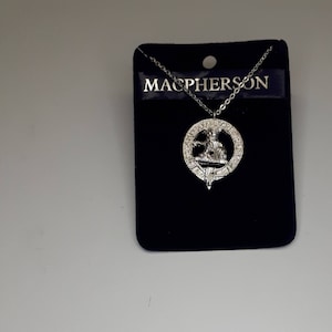 Peut inclure: Collier en argent avec un pendentif en argent représentant un blason avec le mot "MacPherson" sur une carte d'exposition en velours noir.