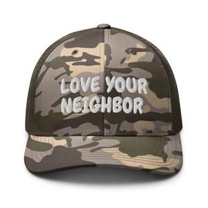 Könnte beinhalten: Eine Camouflage-Trucker-Kappe mit dem Text "LOVE YOUR NEIGHBOR" in weiß gestickt.