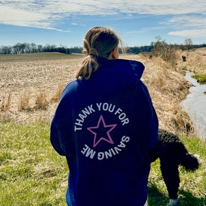 Könnte beinhalten: Ein marineblauer Hoodie mit einem weißen Stern und dem Text "Danke, dass du mich gerettet hast" auf der Rückseite.