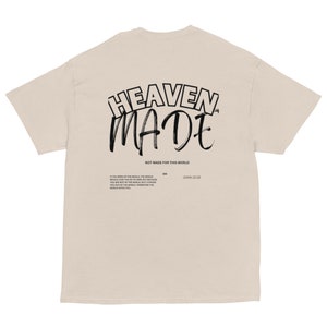 May include: A beige t-shirt with black text that reads "HEAVEN MADE" in a stylised font. Below the text is the phrase "NOT MADE FOR THIS WORLD" and a Bible verse, "JOHN 15:19".