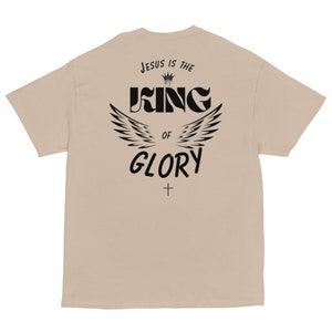 May include: Beige t-shirt with a black graphic print that says "Jesus is the King of Glory" with a crown and wings.