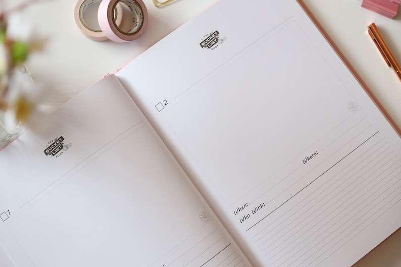 May include: A pink notebook with a black and white logo that says "The Bucket List Book". The notebook has a checklist with the words "When:", "Who with:", and "Where:" written on it.